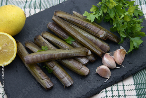 Close-up of some raw razor clams next to some garlic, parsley and lemons on a black slate plate photo