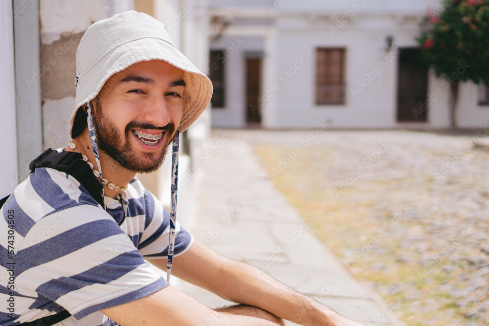 Young latin man looking at camera with a smile while wearing a bucket hat in a colonial neighborhood. Copy space.