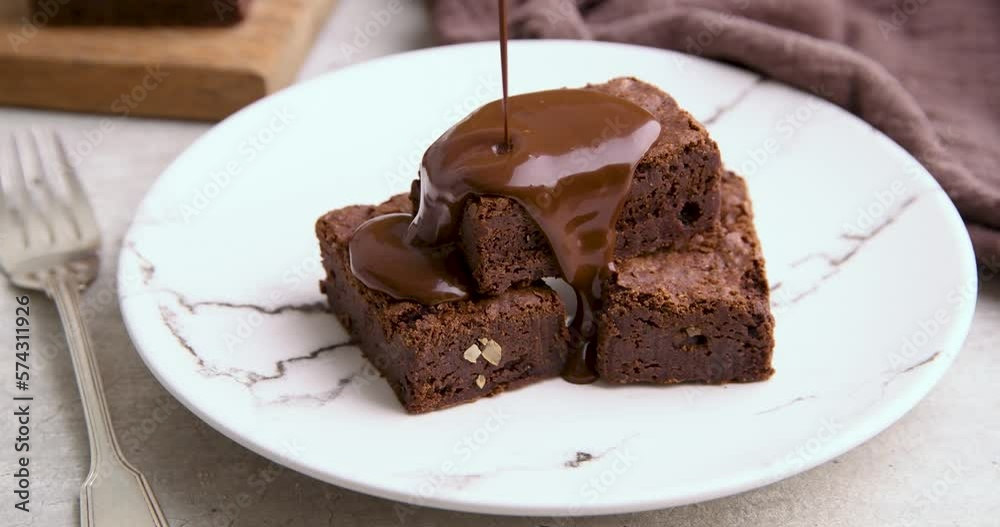 Pouring melted chocolate over pieces of brownie on a white plate Pouring melted chocolate over pieces of brownie on a white plate