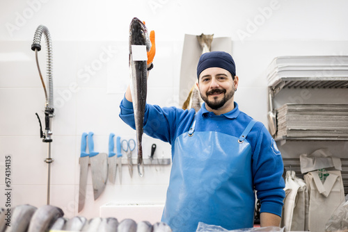 Fotografía A middle-aged fishmonger in apron and hat is teaching the camera a fish, food sales, concept of small and medium enterprises