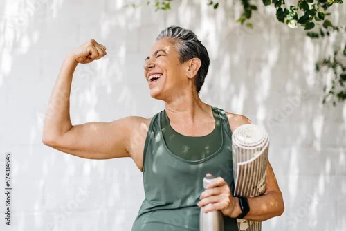 Fototapeta samoprzylepna Elderly woman celebrates her fitness achievements by flaunting her bicep outdoors