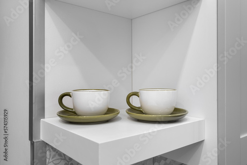 Two ceramic tea cups stand on a shelf