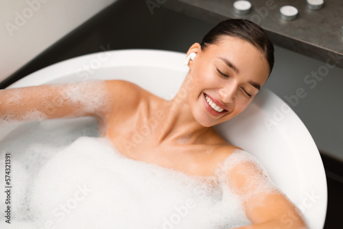 Relaxed Woman Listening Music In Earbuds Lying In Bath Indoors