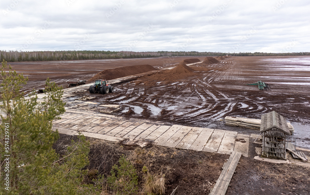 Nature view of a swamp with a peat digging site in a swampy area with a wooden boardwalk and a tractor in the background
