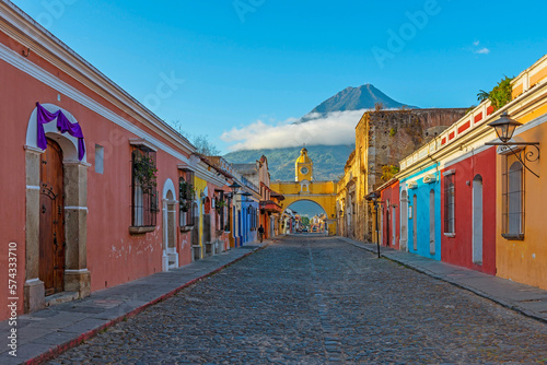 Antigua city main street at sunrise with the yellow arch and the Agua volcano in the background, Guatemala, Central America.