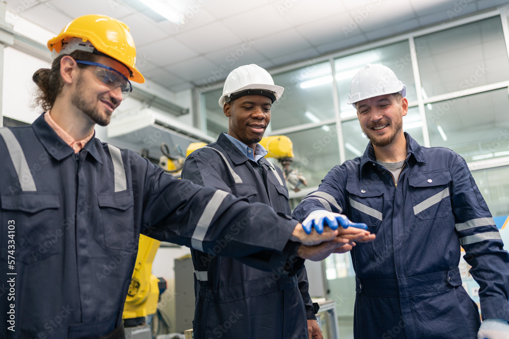 Group of robotic engineers wear helmets safety standing and join hands for ready to work at factory workshop. Technician professional team robot arm welding machine. Group of robotic engineers wear helmets safety standing and join hands for ready to work at factory workshop. Technician professional team robot arm welding machine.
