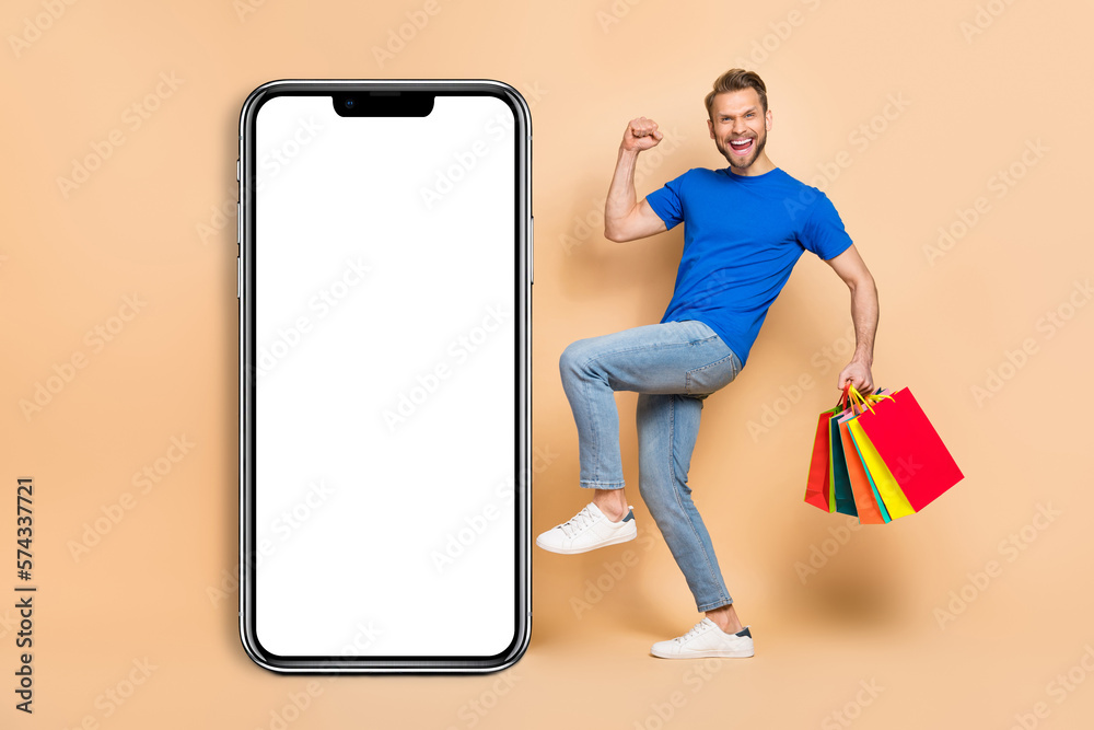 Full size photo of delighted person raise fist hold packages empty space display isolated on beige color background Full size photo of delighted person raise fist hold packages empty space display isolated on beige color background