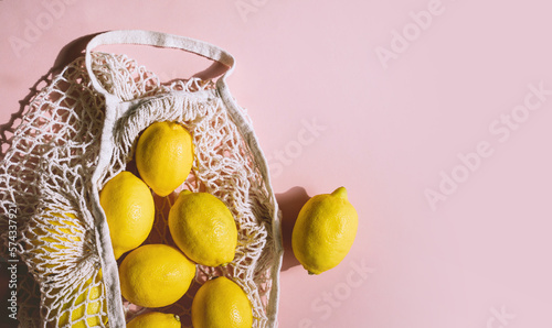 Fototapeta Naklejka Na Ścianę i Meble -  Photo of organic lemon fruits in mesh bag on light pink background. Perfectly imperfect lemons pattern. Natural food. Trendy sunlight, minimal style.