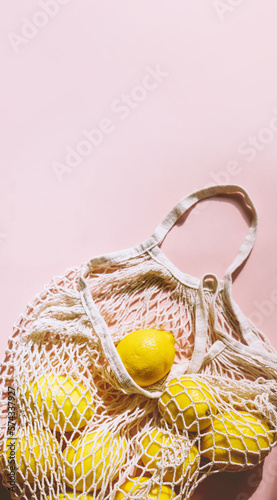 Photo of organic lemon fruits in mesh bag on light pink background. Perfectly imperfect lemons pattern. Natural food. Trendy sunlight, minimal style.