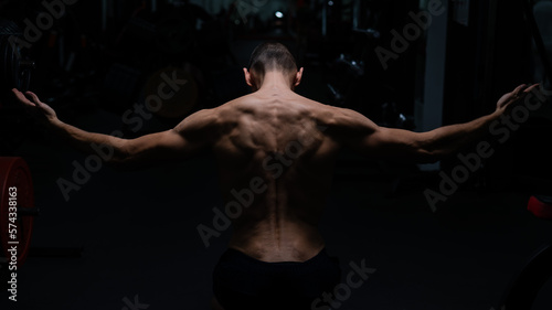 Back view of shirtless man with sculpted body in gym. 
