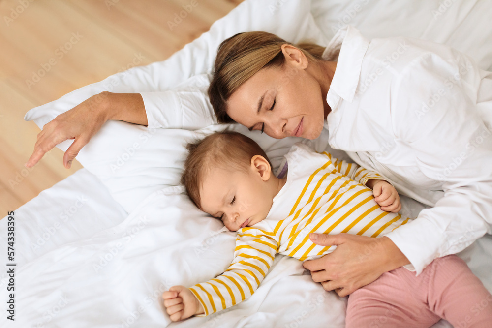 Mother and little baby infant girl lying sleeping together in cozy white bed at home, above view, free space Mother and little baby infant girl lying sleeping together in cozy white bed at home, above view, free space