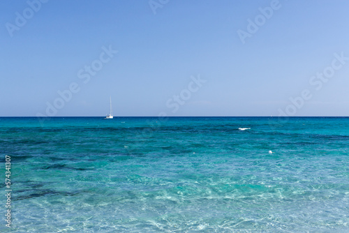 Clear blue turquoise water of Mediterranean sea and sailboat anchored near the coast at Sardinia, Italy on sunny day.