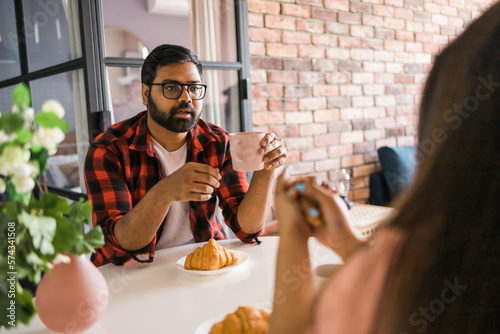 Young diverse loving couple eating croissant and talks together at home in breakfast time. Communication and relationship concept photo