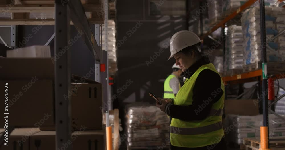 4k slow-motion video of the female warehouse manager using the mobile phone to scan the boxes while sorting the storage. The coworkers can be seen in the background doing their work. 4k slow-motion video of the female warehouse manager using the mobile phone to scan the boxes while sorting the storage. The coworkers can be seen in the background doing their work.