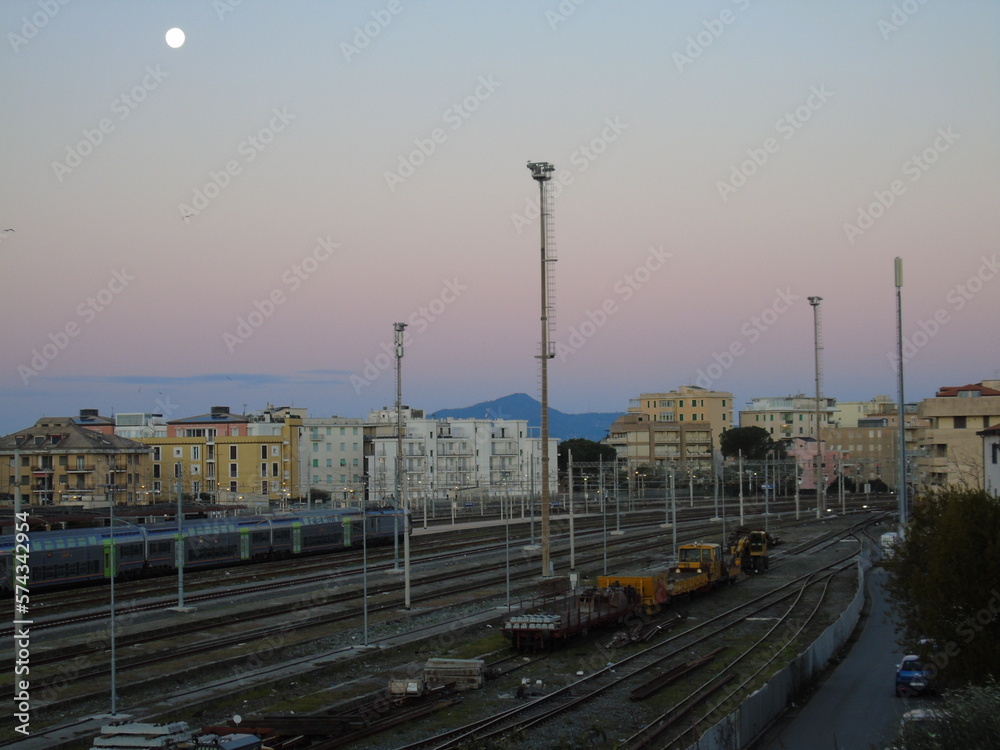 Sestri Levante, Italy - February 07, 2023: Almost full moonlight over the station of Sestri in winter days. Beautiful sunset hidden behind the mountains. Moon over the city by day.