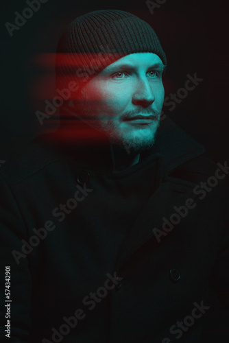 Man with winter hat and black coat studio portrait. Model with beard looking aside the camera with serious look. Red and blue color split effect style. 3D glitch virtual reality effect
