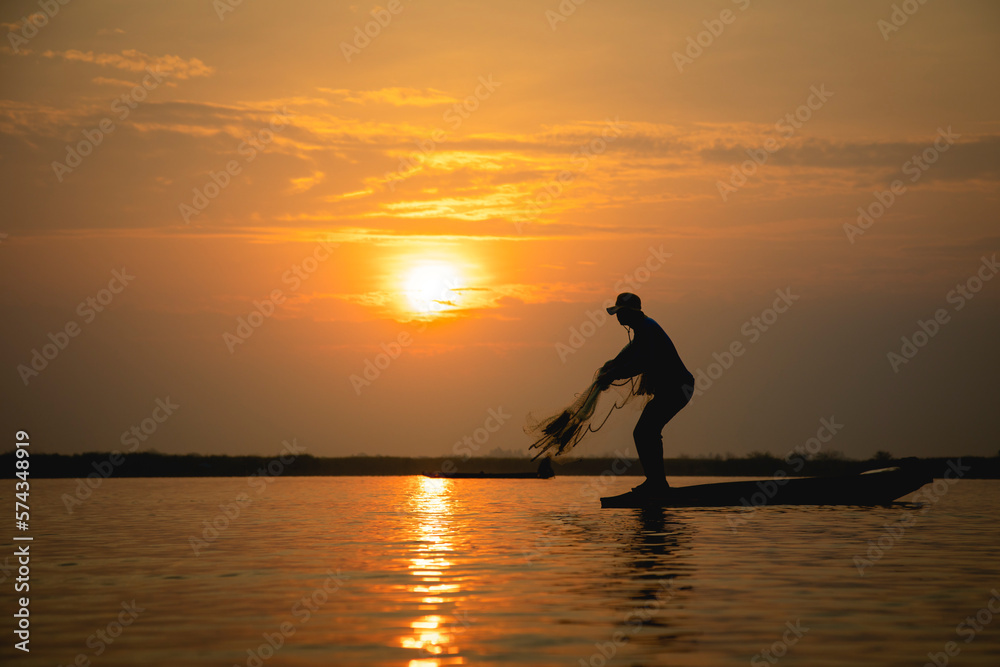 Silhouette of fisherman throwing fishing net during sunrise at lake, Asian Thailand