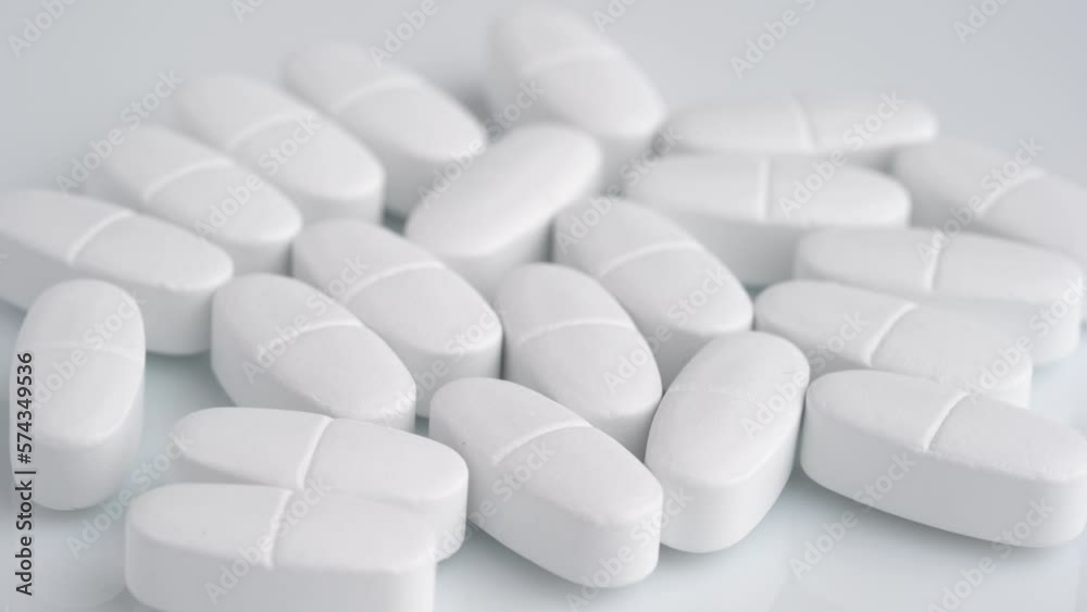 White oblong tablets with a dividing strip rotate macro. White oblong tablets with a dividing strip rotate macro.