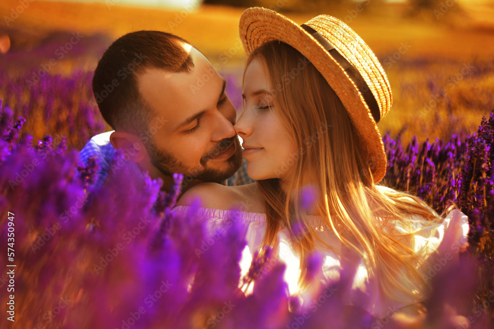 A couple in love in a field of lavender at sunset in good weather. Beautiful woman in a dress and straw panama with a man on the background of nature, love and feelings. Blue, purple lavende.