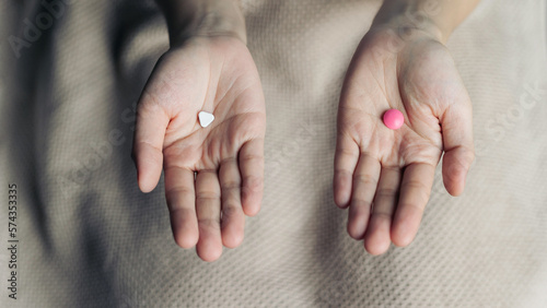 Female hands hold and offer two choice medicine pills capsule for chosen. White and pink candy or meds compare to choose from. Concept decision making or indecisiveness.