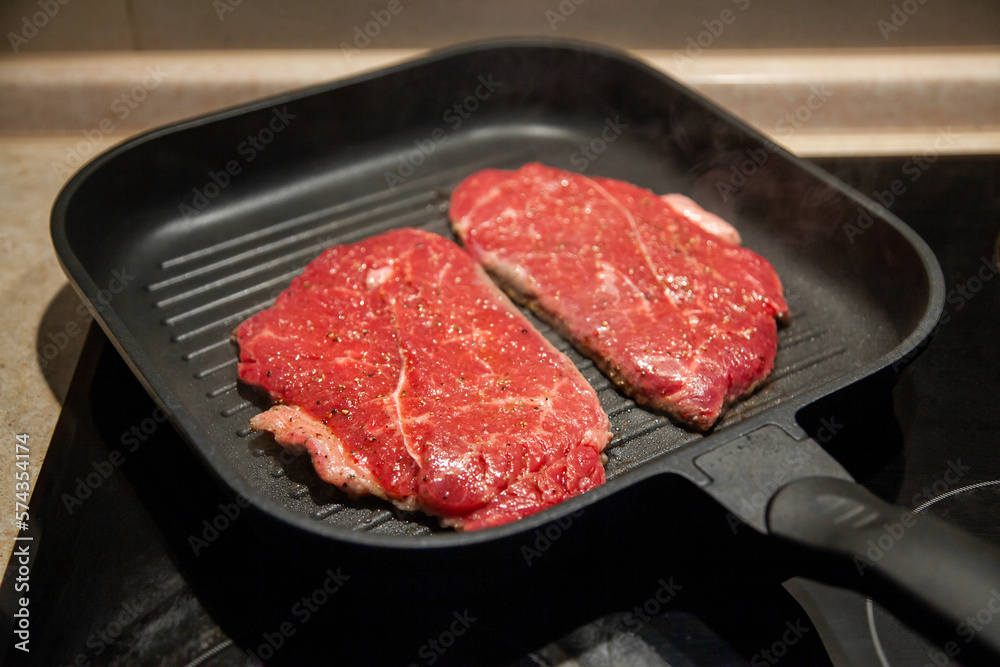 Raw minute steak of marbled beef in a grill pan on an electric cooking surface