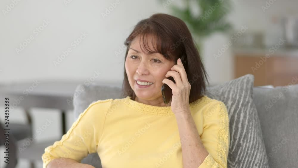 Attractive middle age woman long hair wearing yellow top smiling talking on mobile phone sitting at comfortable morning home dining table Attractive middle age woman long hair wearing yellow top smiling talking on mobile phone sitting at comfortable morning home dining table
