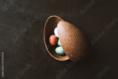 Photography Cracked easter chocolate egg  full with small chocolate eggs on black background