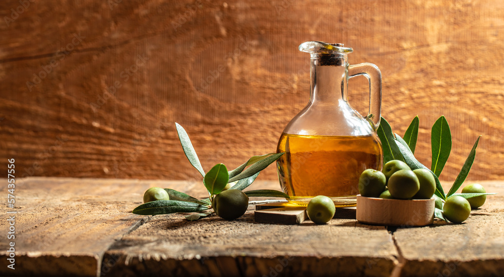Glass container with olive oil branches and olives on a wooden background. Long banner format Glass container with olive oil branches and olives on a wooden background. Long banner format