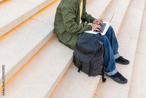 Anonymous student with backpack using laptop on stairs photo