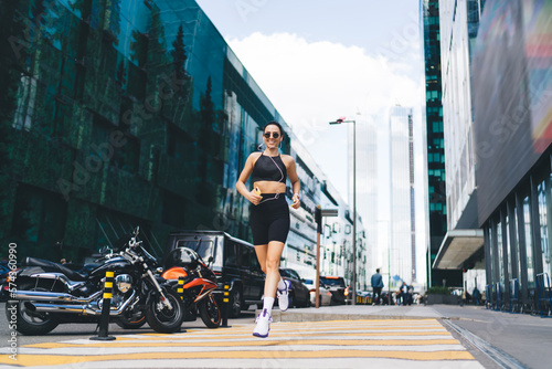 Cheerful sportswoman jogging on crosswalk in city