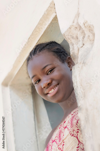 Young Afro girl standing at the door of her house, smiling expression, photo, low-angle view