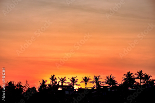 Orange-colored sunset sunrise view with coconut tree and house as a shadow in the background