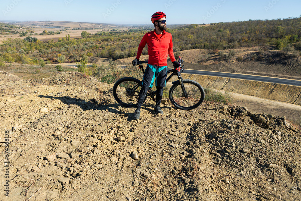 Cyclist riding bicycle on offroad against clear sky. A man in an outfit stands with a bicycle on an autumn sunny day.