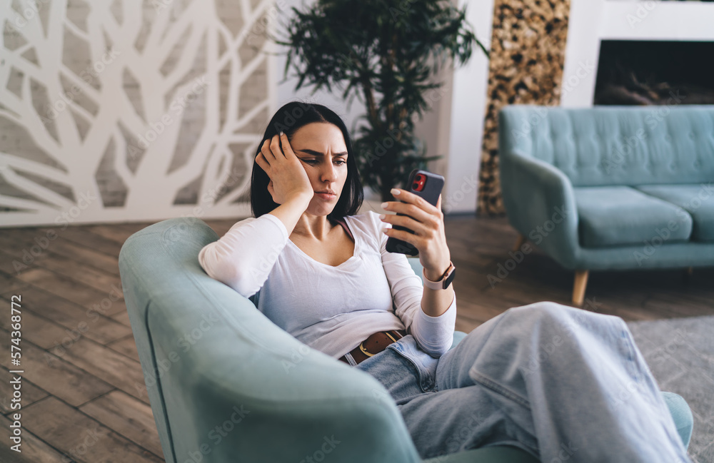 Obraz premium Tired female watching boring video on smartphone