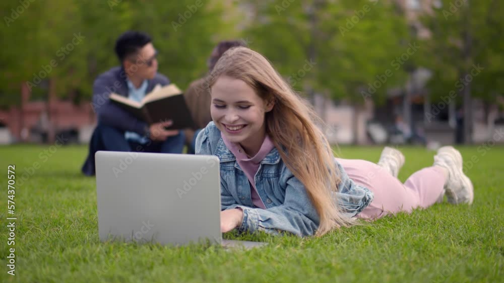 Attractive young female using laptop while sitting on green grass of campus lawn. Realtime Attractive young female using laptop while sitting on green grass of campus lawn. Realtime