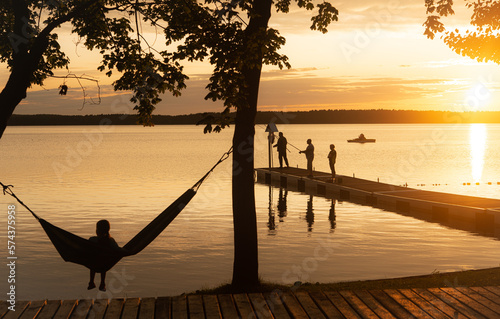 Summer sunset by the calm lake with people relaxing on jetty, copy space photo