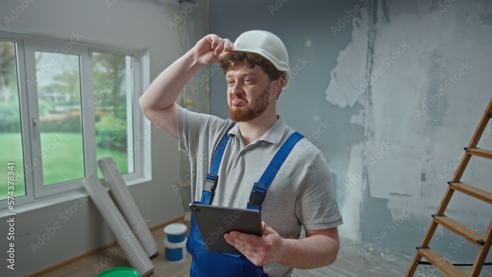 Male foreman is planning renovation project in an apartment using tablet. Redhead master man thinking, viewing and visualizing ideas against background of apartment in process of renovation. Male foreman is planning renovation project in an apartment using tablet. Redhead master man thinking, viewing and visualizing ideas against background of apartment in process of renovation.