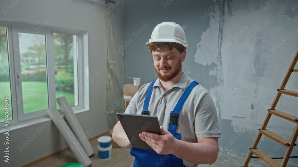 Male foreman is planning renovation project in an apartment using tablet. Redhead master man thinking, viewing and visualizing ideas against background of apartment in process of renovation. Male foreman is planning renovation project in an apartment using tablet. Redhead master man thinking, viewing and visualizing ideas against background of apartment in process of renovation.