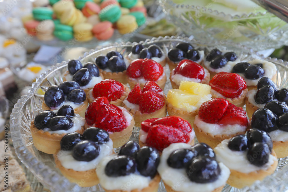 Colored mini tarts with strawberry, ananas and grapes on a table.