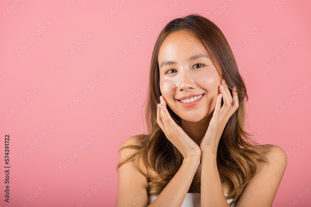 Eye skin treatment. Asian beautiful young woman smiling mask cosmetic patches gel under the eyes, Portrait female with natural makeup hydrogel eye patch on face, isolated on pink background, skincare Eye skin treatment. Asian beautiful young woman smiling mask cosmetic patches gel under the eyes, Portrait female with natural makeup hydrogel eye patch on face, isolated on pink background, skincare