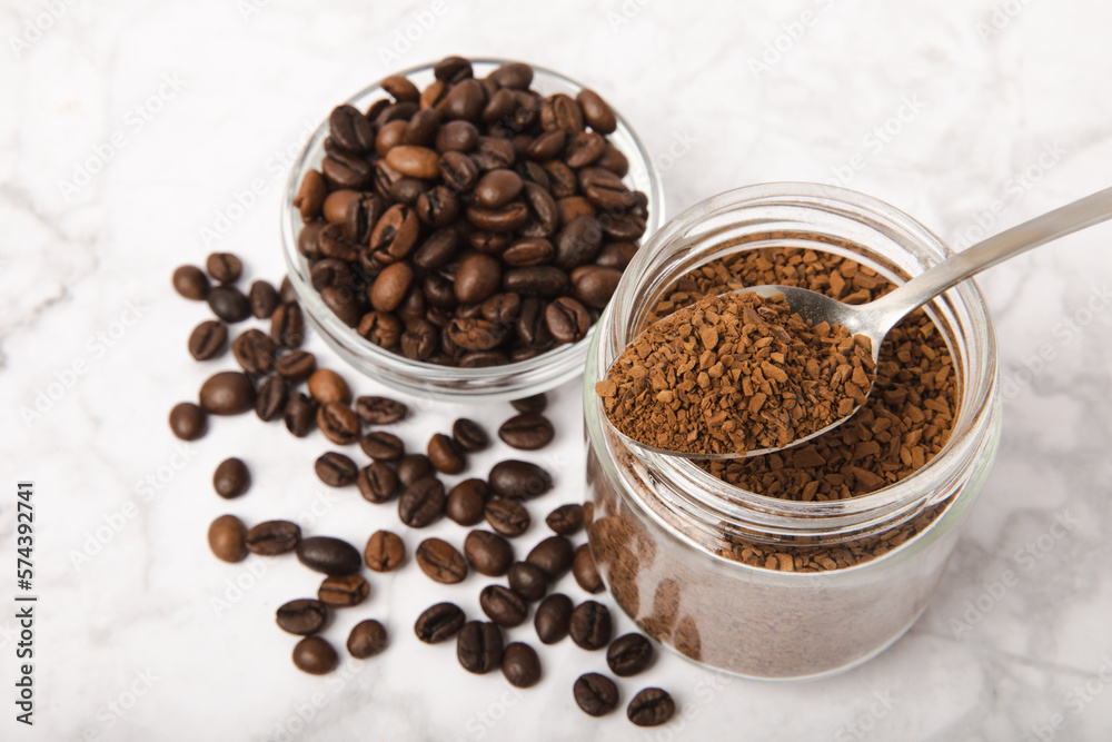Instant coffee beans in a glass jar on a white marble background. Hot drink ingredients. Instant coffee on the table. Espresso. Place for text. Place to copy. Banner. Instant coffee beans in a glass jar on a white marble background. Hot drink ingredients. Instant coffee on the table. Espresso. Place for text. Place to copy. Banner.