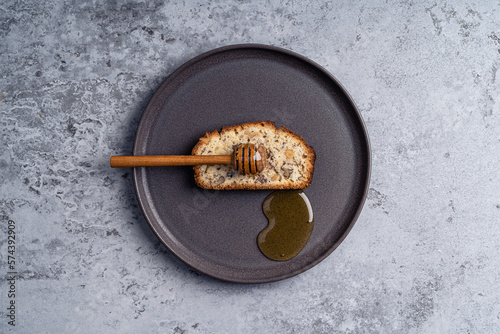 Slice of cake with walnuts and honey dipper on plate on gray background, top view
