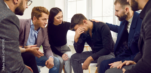 Team of supportive, understanding people, friends, co workers sitting in a circle in the office workplace and comforting a sad man who is showing emotions and crying. Support concept Banner background