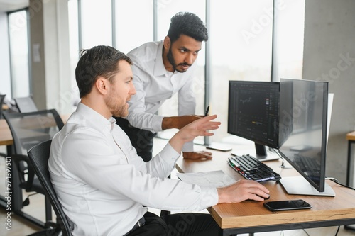 Two men traders sitting at desk at office together looking at data analysis discussing brainstorming successful strategy inspired teamwork concept close-up