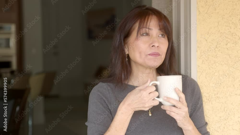 Close up attractive woman long hair black top standing at back door holding coffee cup drinking looking around Close up attractive woman long hair black top standing at back door holding coffee cup drinking looking around