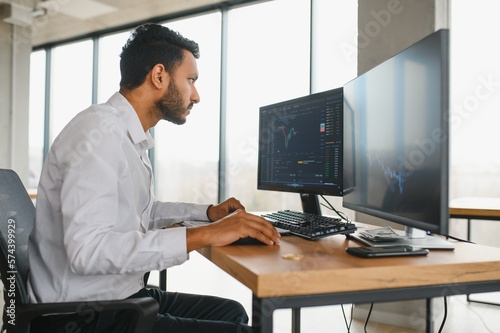 Portrait of a positive successful Indian or Arabian trader, stock market broker, Crypto charts on laptop screen