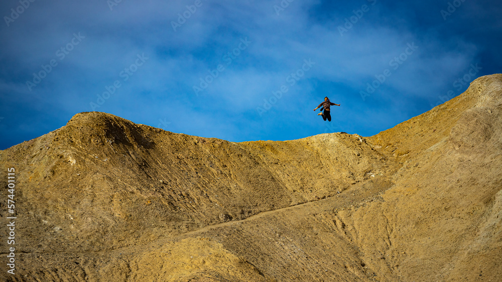 A happy, adventurous brave girl jumps high above a mountain ridge in Golden Canyon Trail, Death Valley, California, USA 