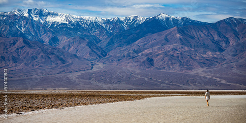 pretty girl in white lace dress walking in badwater basin in death valley ndational park, california, usa; spring in death valley, huge mountains in the background