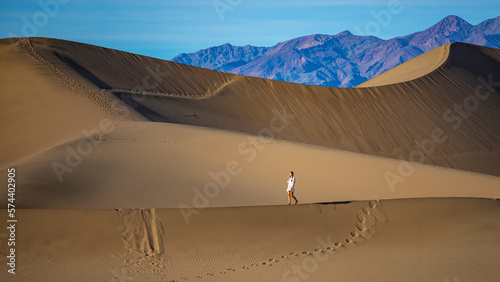 girl in white dress lost in the desert; walking on large sand dunes in mesquite flat sand dunes in death valley national park, california, usa