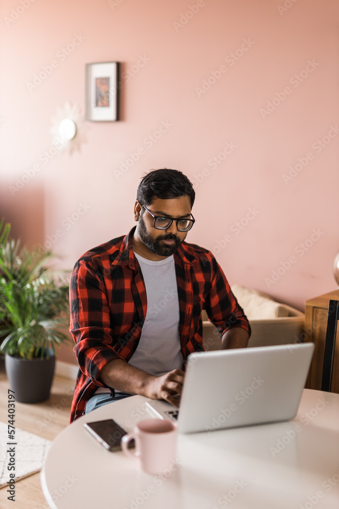 technology remote job and lifestyle concept - happy indian man in glasses with laptop computer working at home office technology remote job and lifestyle concept - happy indian man in glasses with laptop computer working at home office